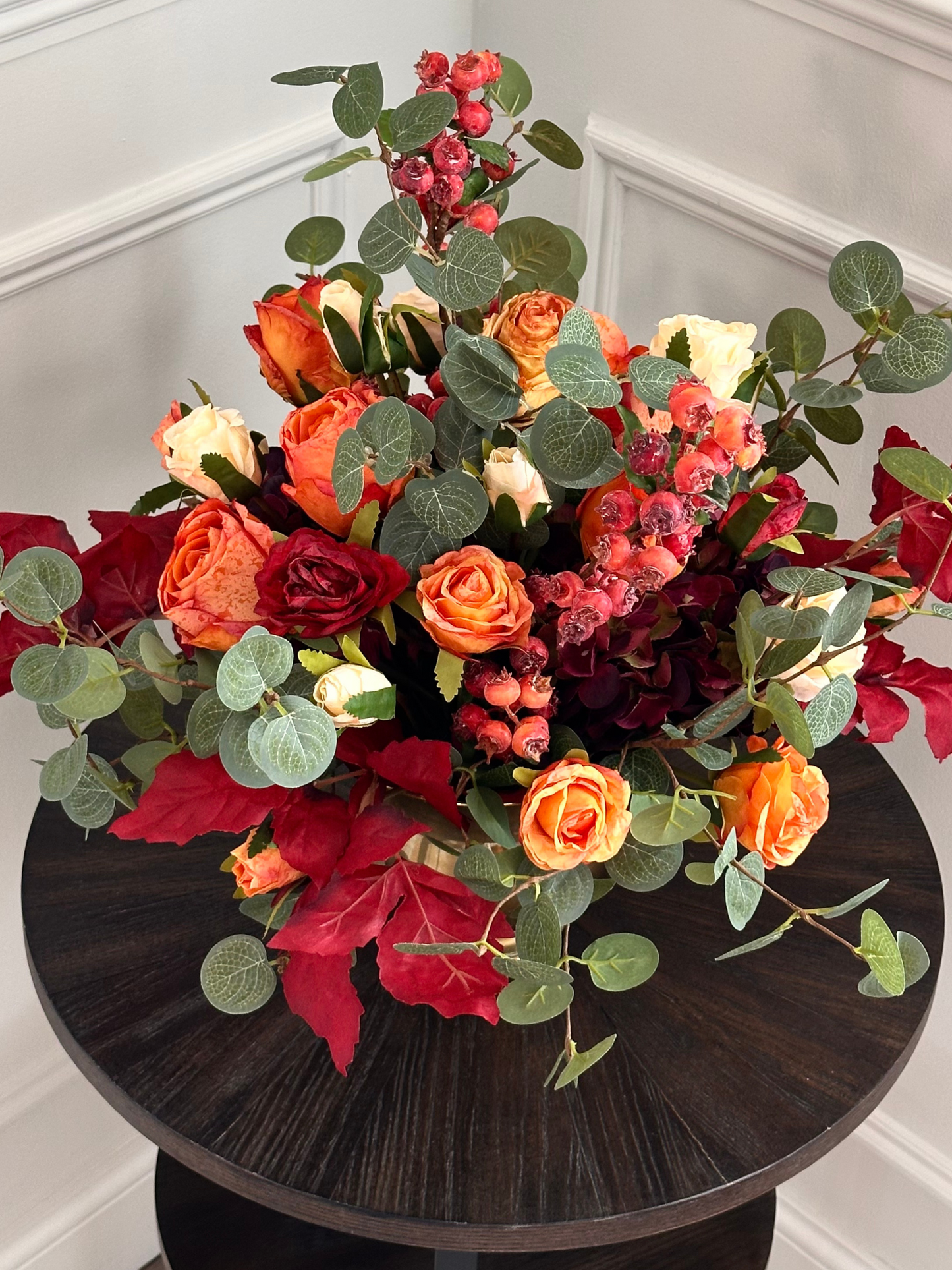 Bouquet of autumn colorful flowers on a dark wooden table against a white wall.