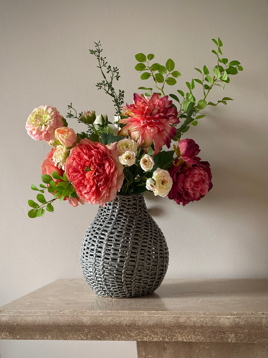 Red Floral artificial arrangement in a textured vase on a stone surface with a neutral background