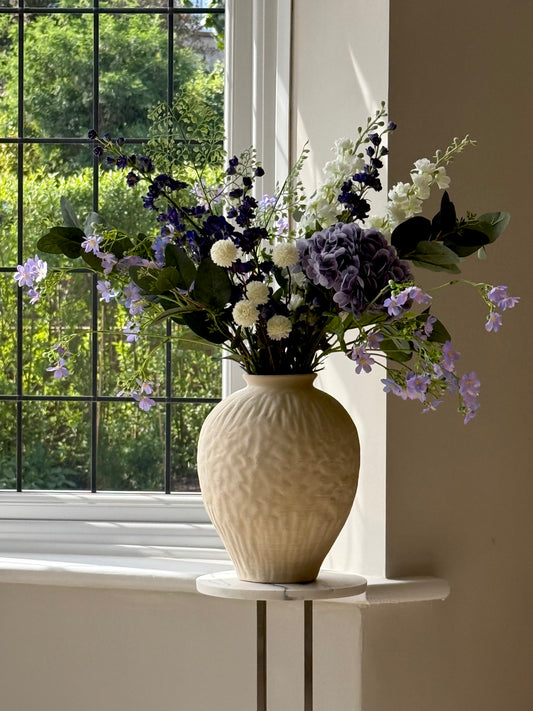 Vase with flowers on a windowsill with a view of greenery outside