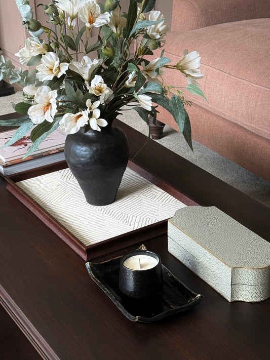 Decorative coffee table setting with a vase of flowers, candle, and box on a wooden surface.