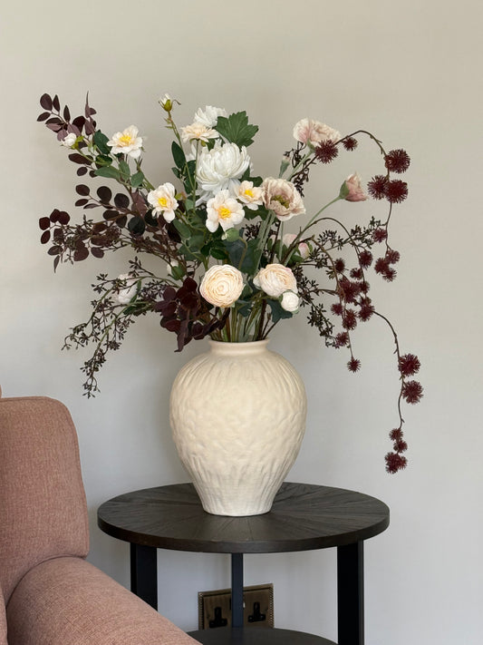 Floral arrangement on a table next to a textured wall and chair.