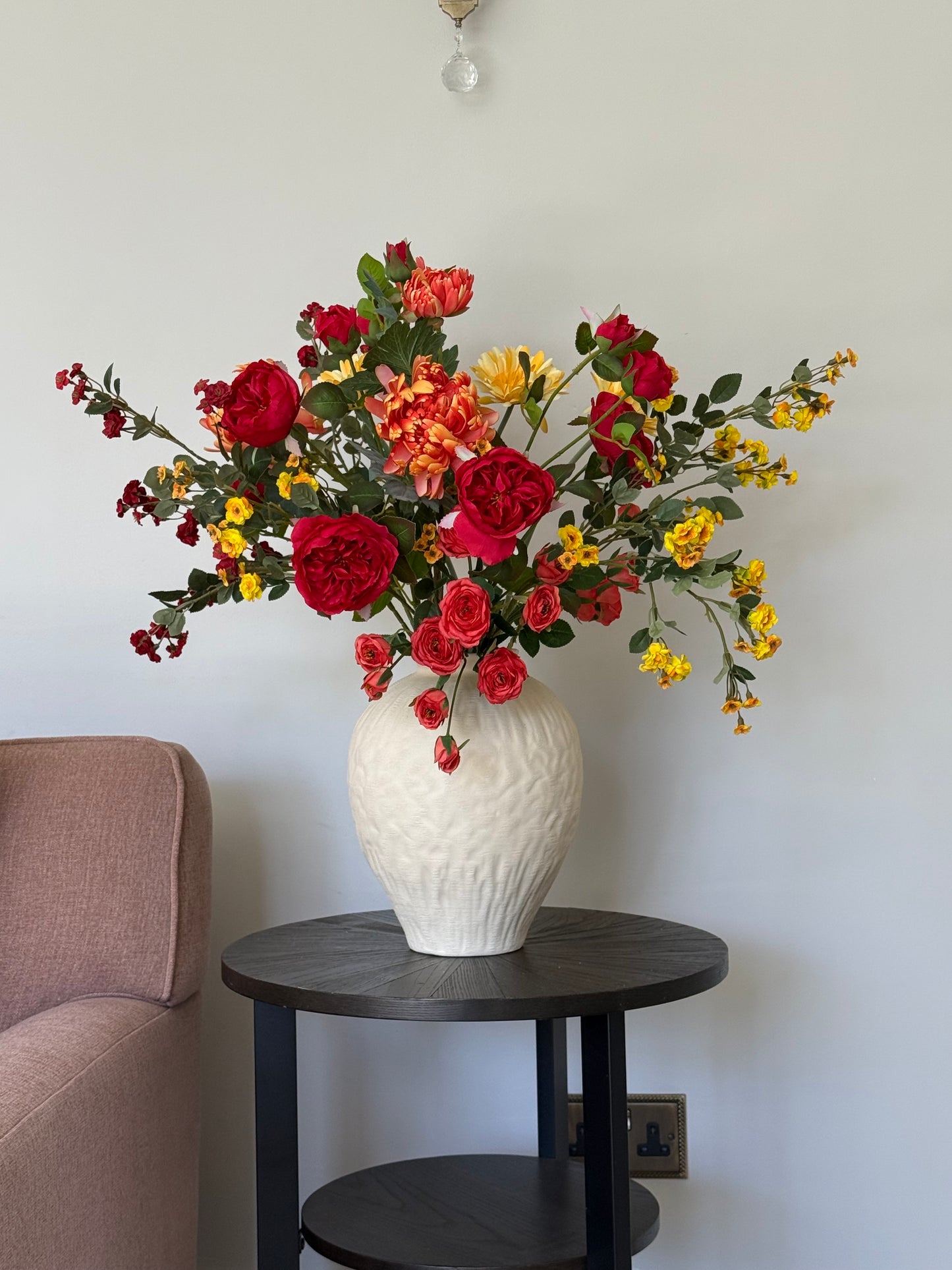 Colorful bouquet of flowers on a table with a white lamp and chair in the background.