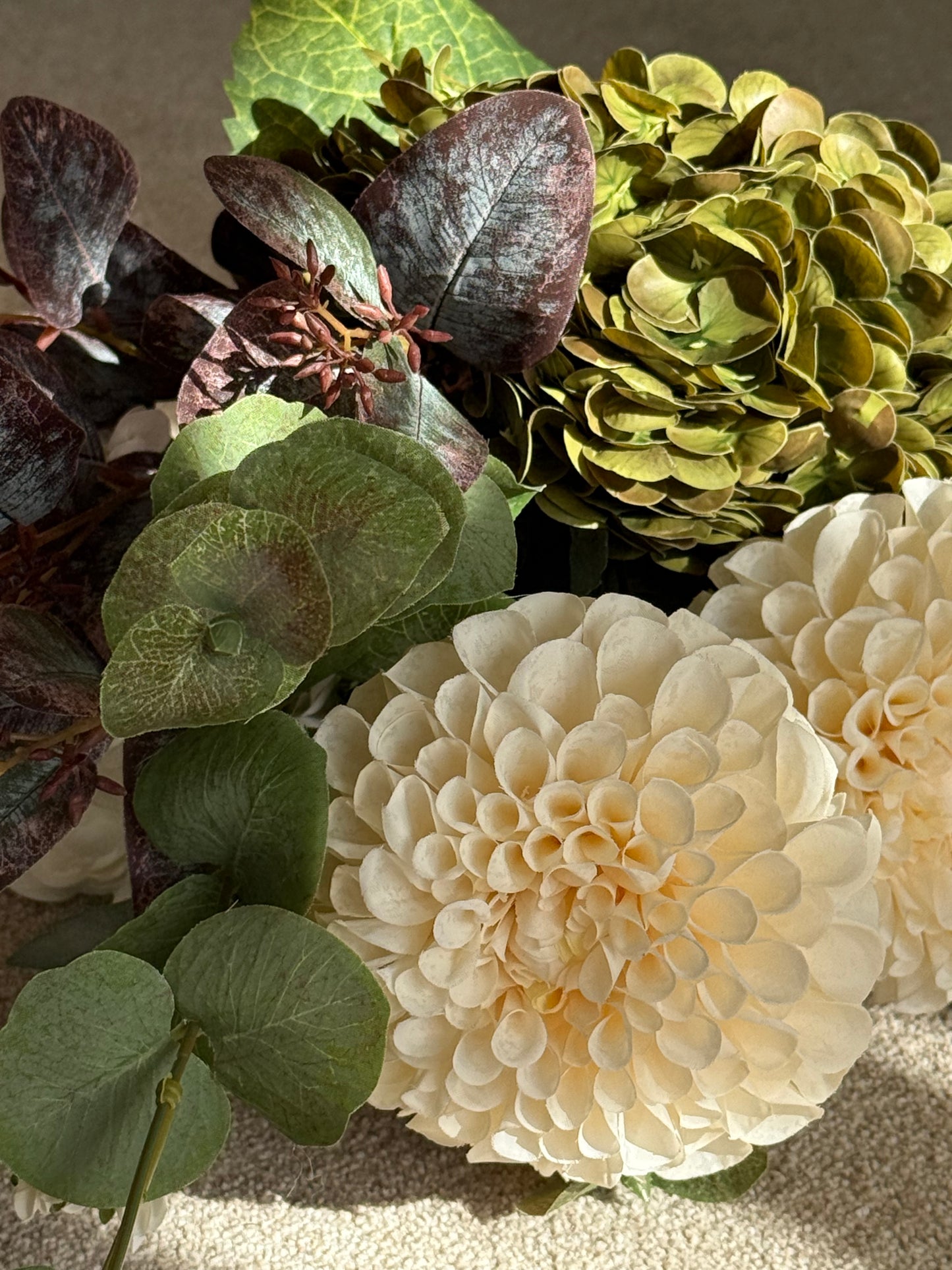 Close-up of a bouquet with cream flowers, green leaves, and hydrangea.