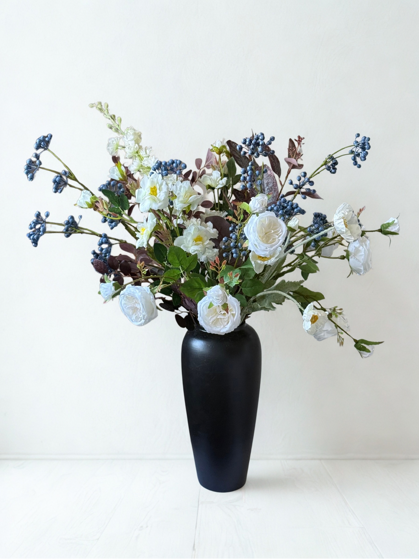 Black vase with a bouquet of white and blue flowers on a white background