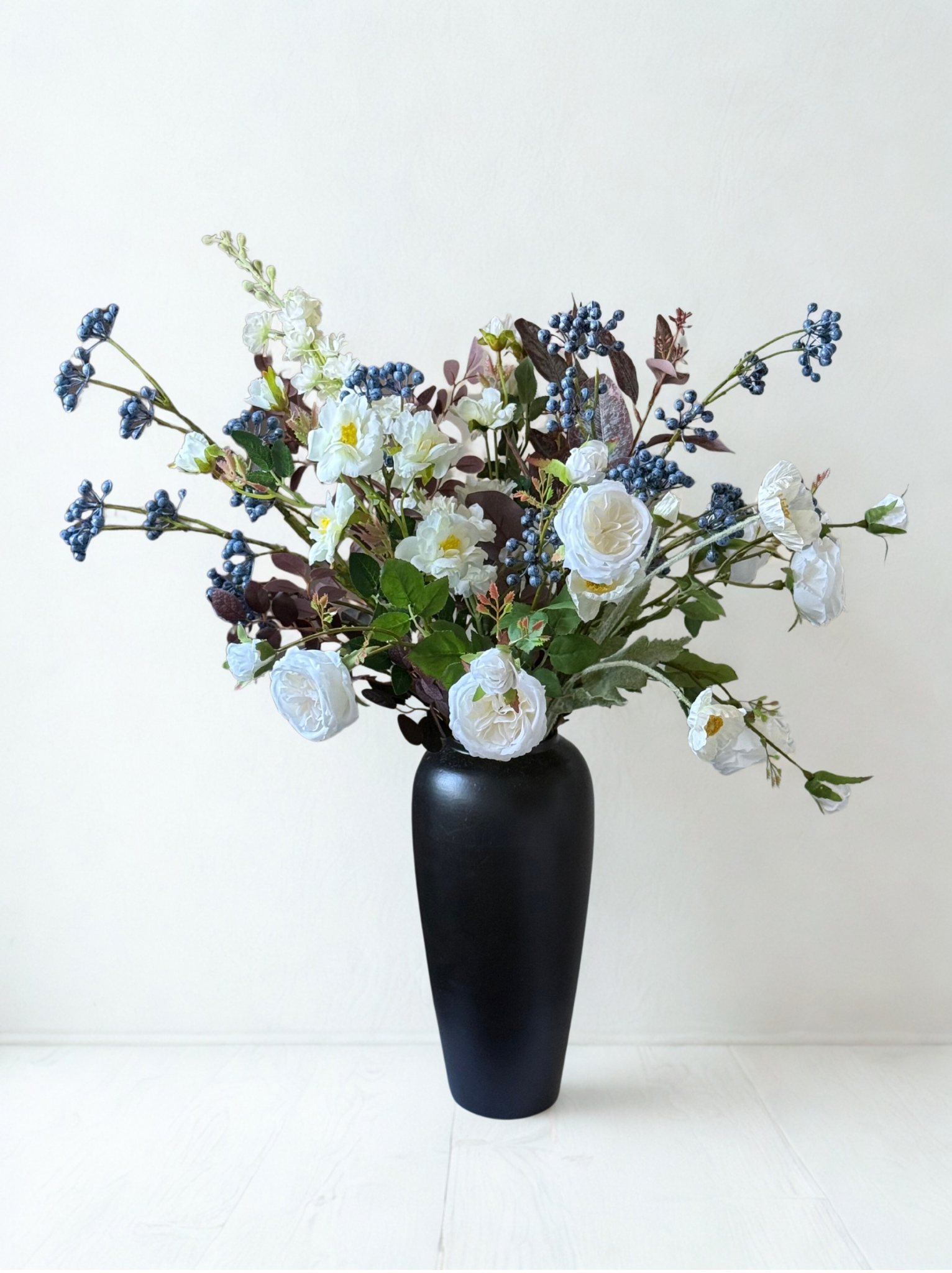 Black vase with a bouquet of white and blue flowers on a white background