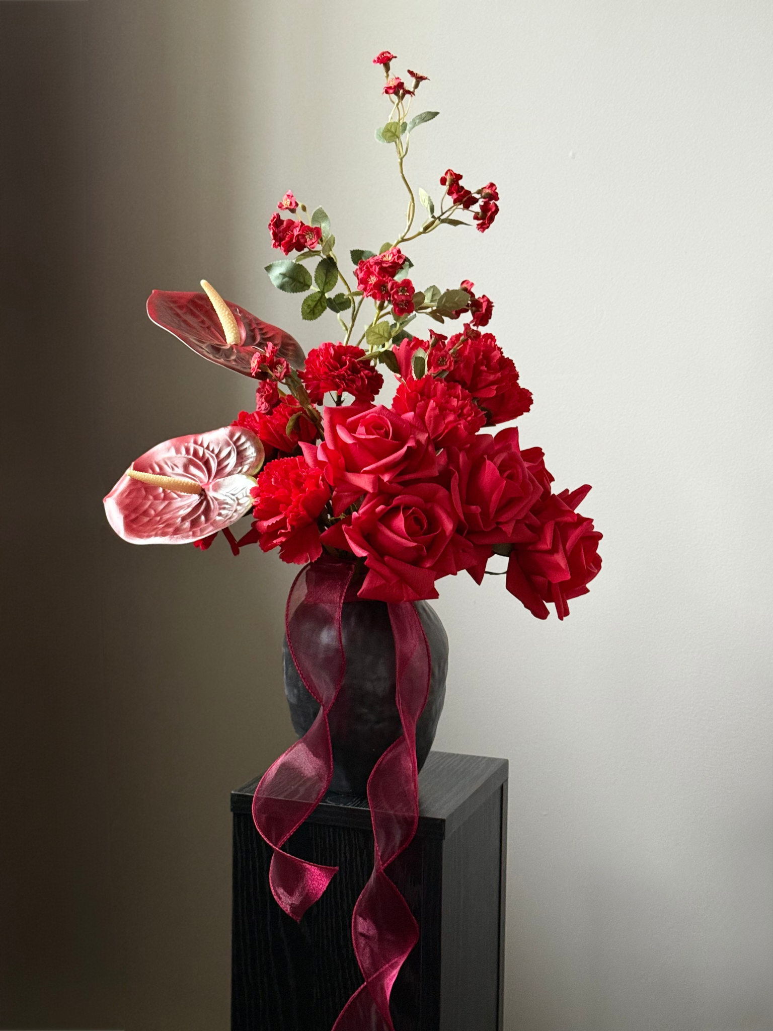 Vase with red faux roses and pink ribbon on a dark surface against a gray background