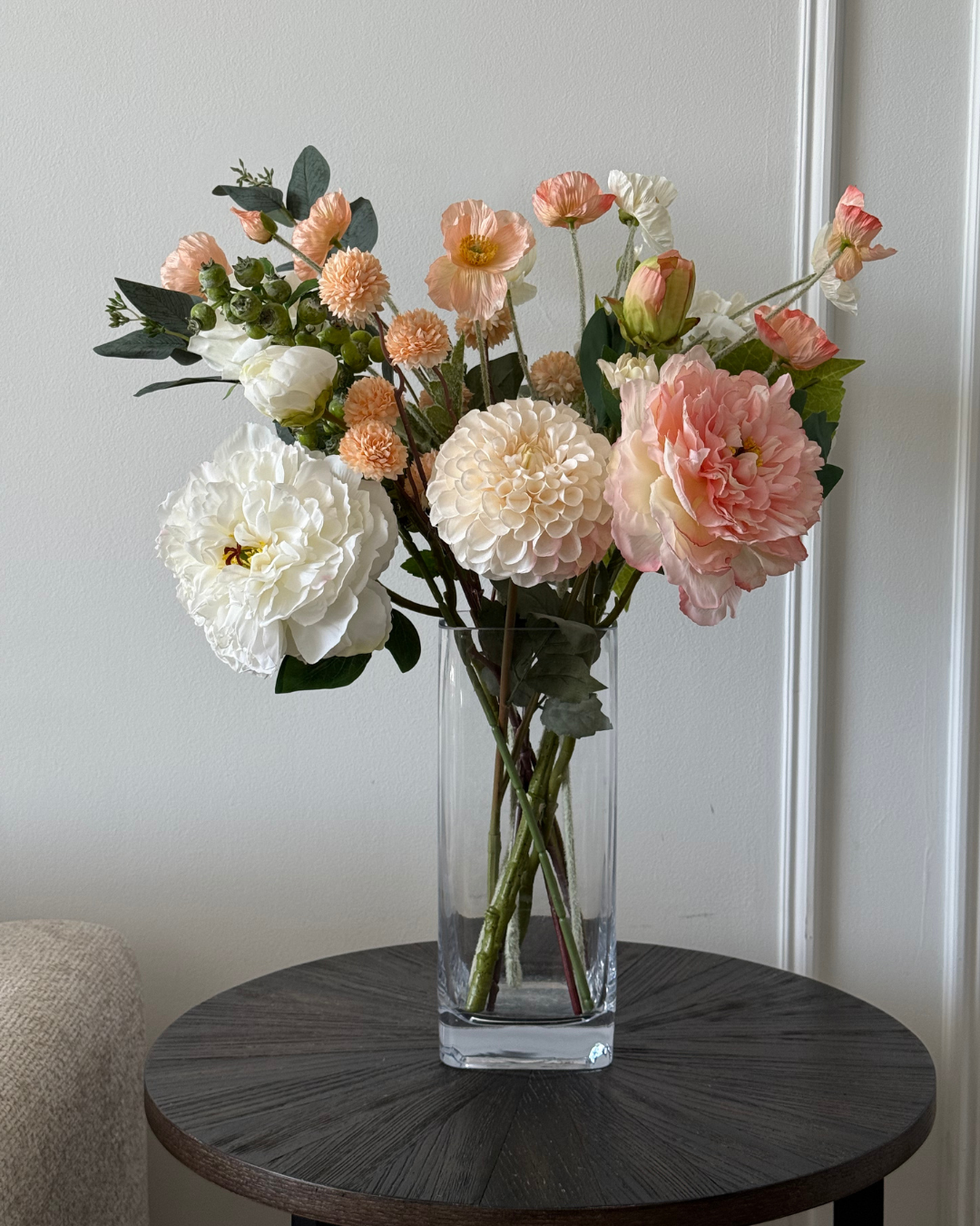 Clear vase with artificial Best & Bloom pink and white flowers on a wooden table against a white wall