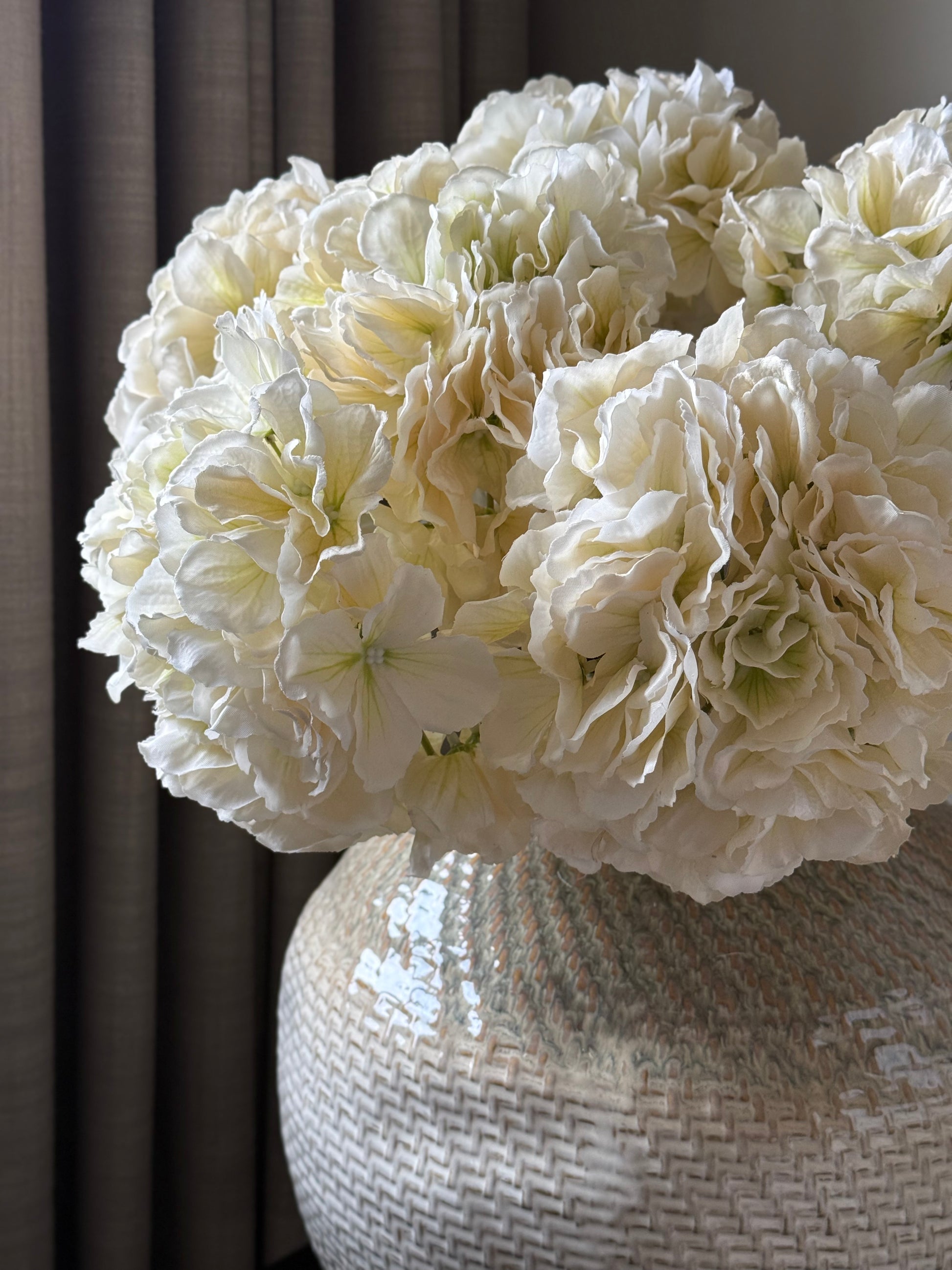 White artificial hydrangea flowers in a textured vase against a neutral background