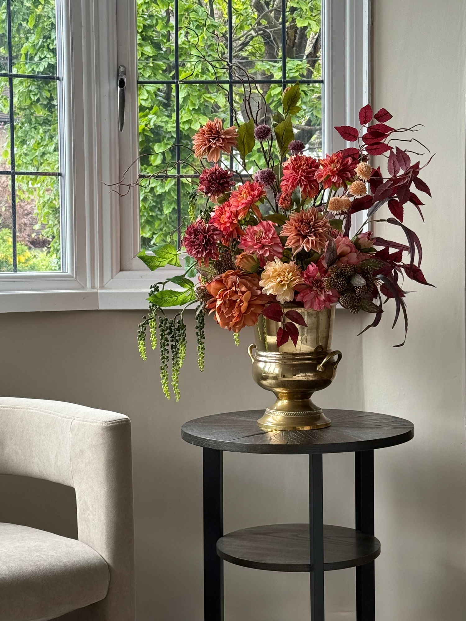 Floral arrangement in a gold vase on a black side table by a window