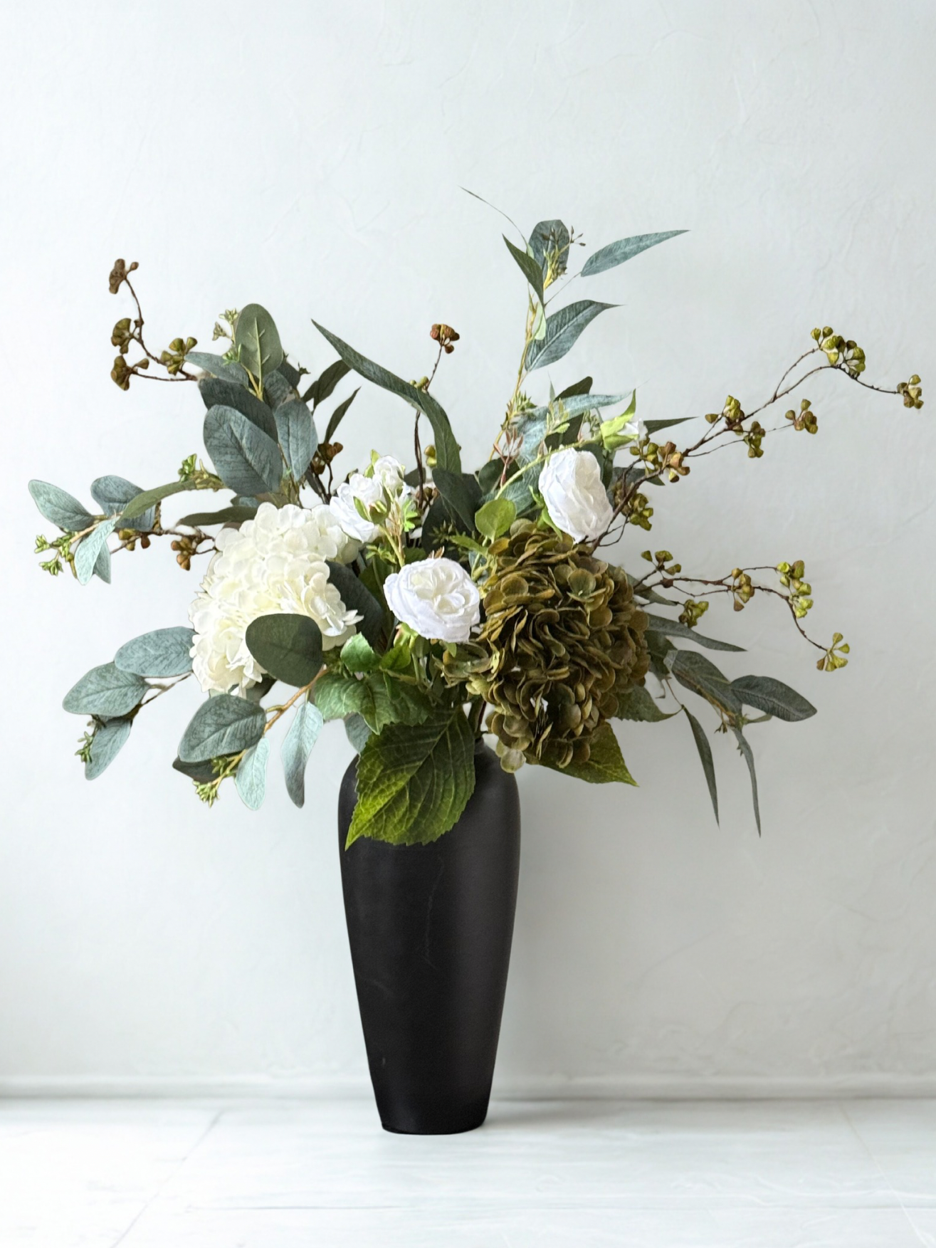 Artificial Neutral Green Floral arrangement in a black vase on a white background