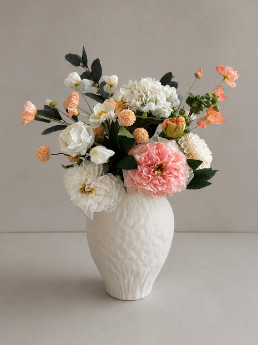 cream ceramic vase with a bouquet of pink and white flowers on a light grey background