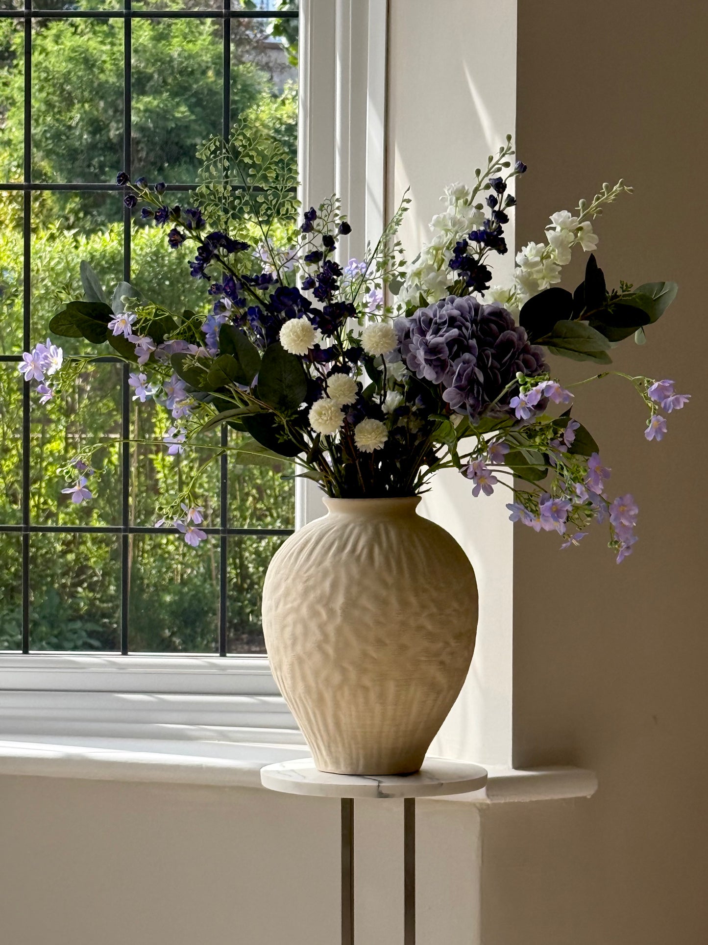 Vase with flowers on a windowsill with a view of greenery outside
