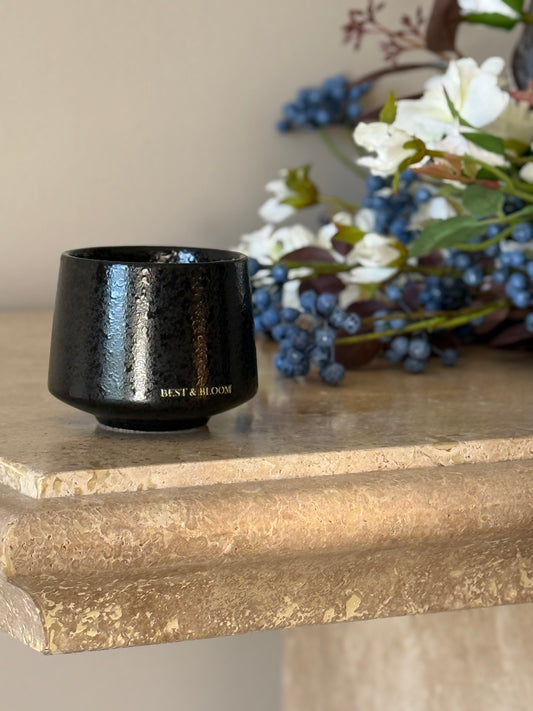 Black ceramic candle on a stone surface with flowers in the background