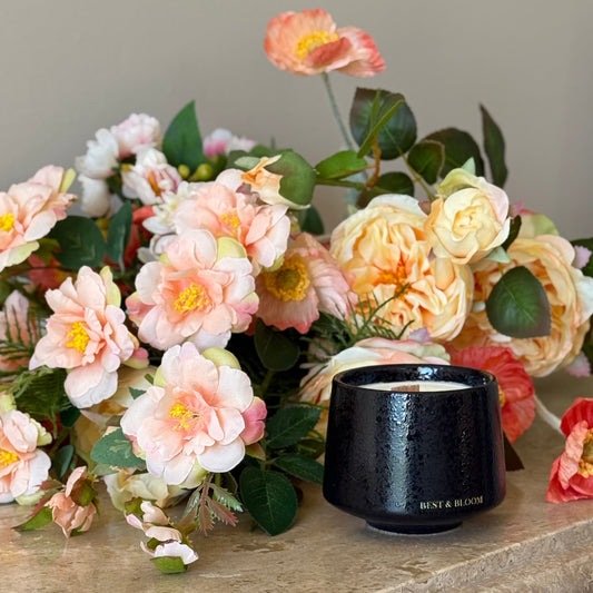 Black candle on a stone surface with pink and white flowers in the background