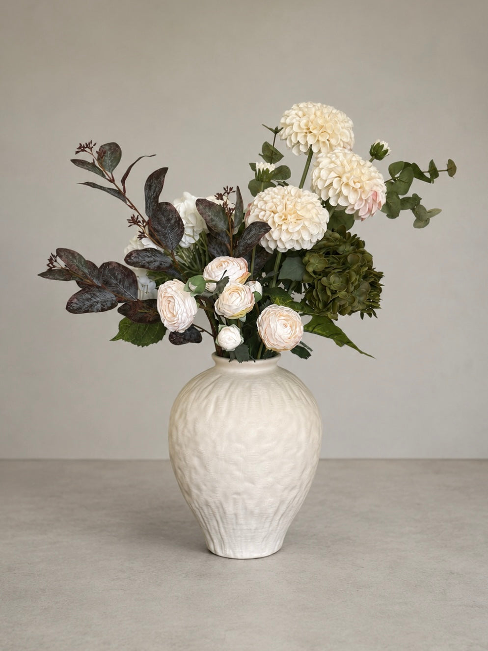 White textured vase with a bouquet of faux dahlia flowers on a neutral background