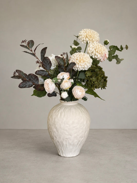 White textured vase with a bouquet of faux dahlia flowers on a neutral background