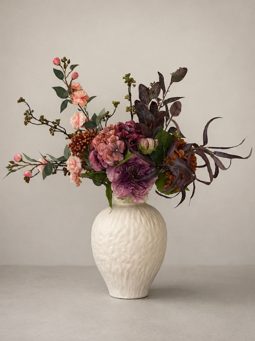 White textured vase with a bouquet of flowers on a plain background