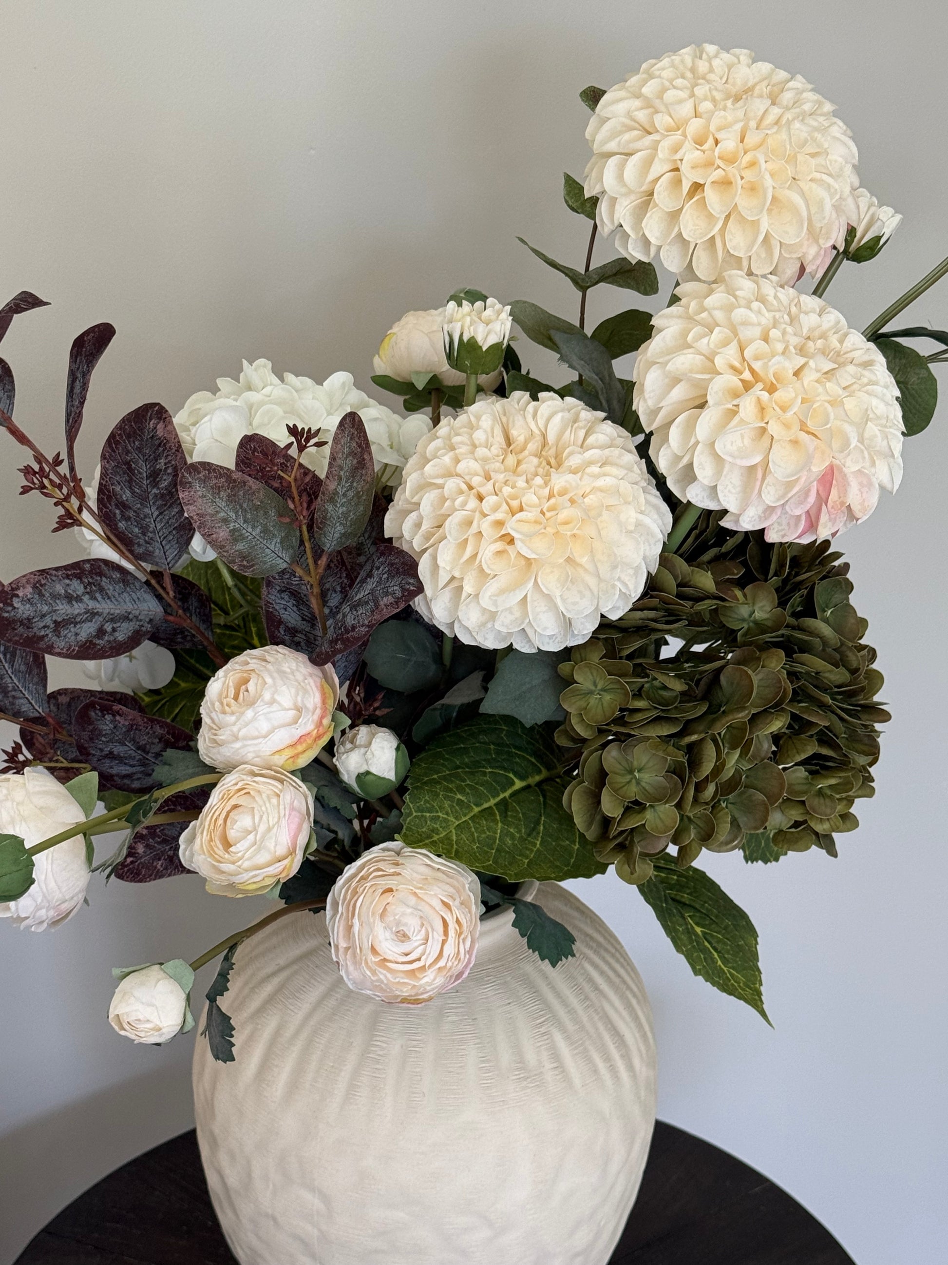 Bouquet of white dahlias and green flowers with a textured vase on a light background