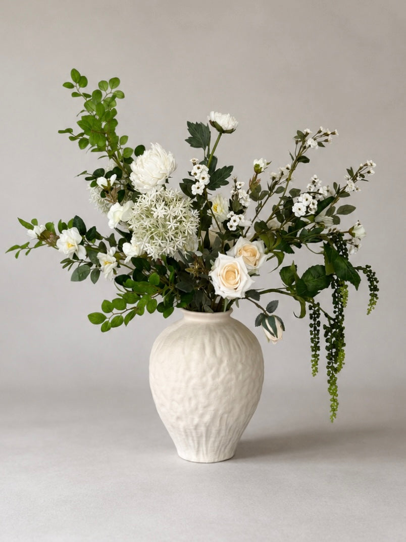 White vase with a bouquet of white faux flowers on a gray background