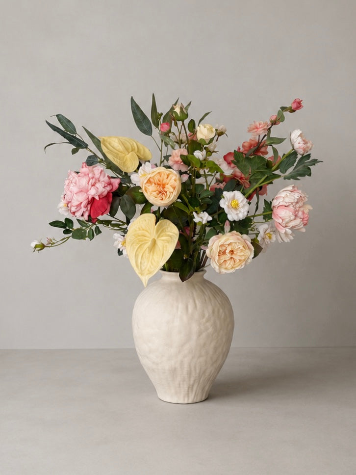White vase with a bouquet of peachy artificial flowers on a gray background