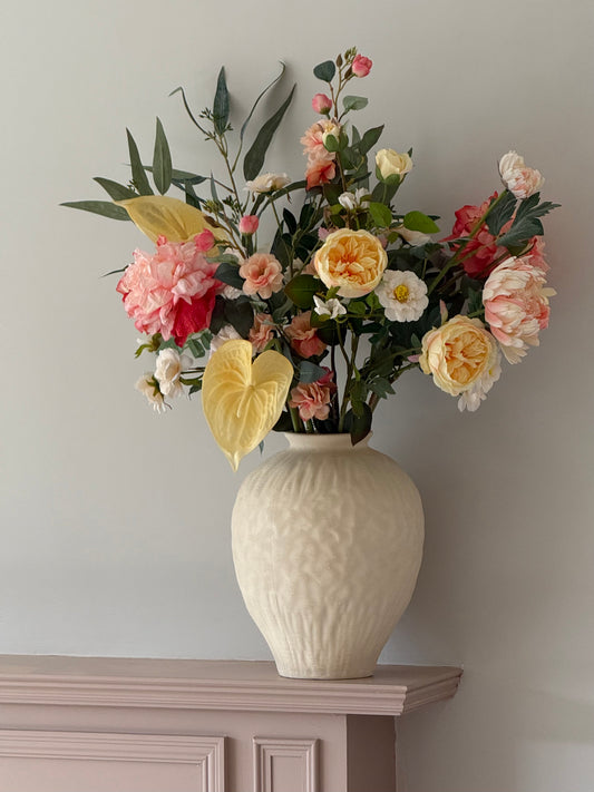 Faux Floral arrangement in a textured vase on a wooden surface with a neutral background