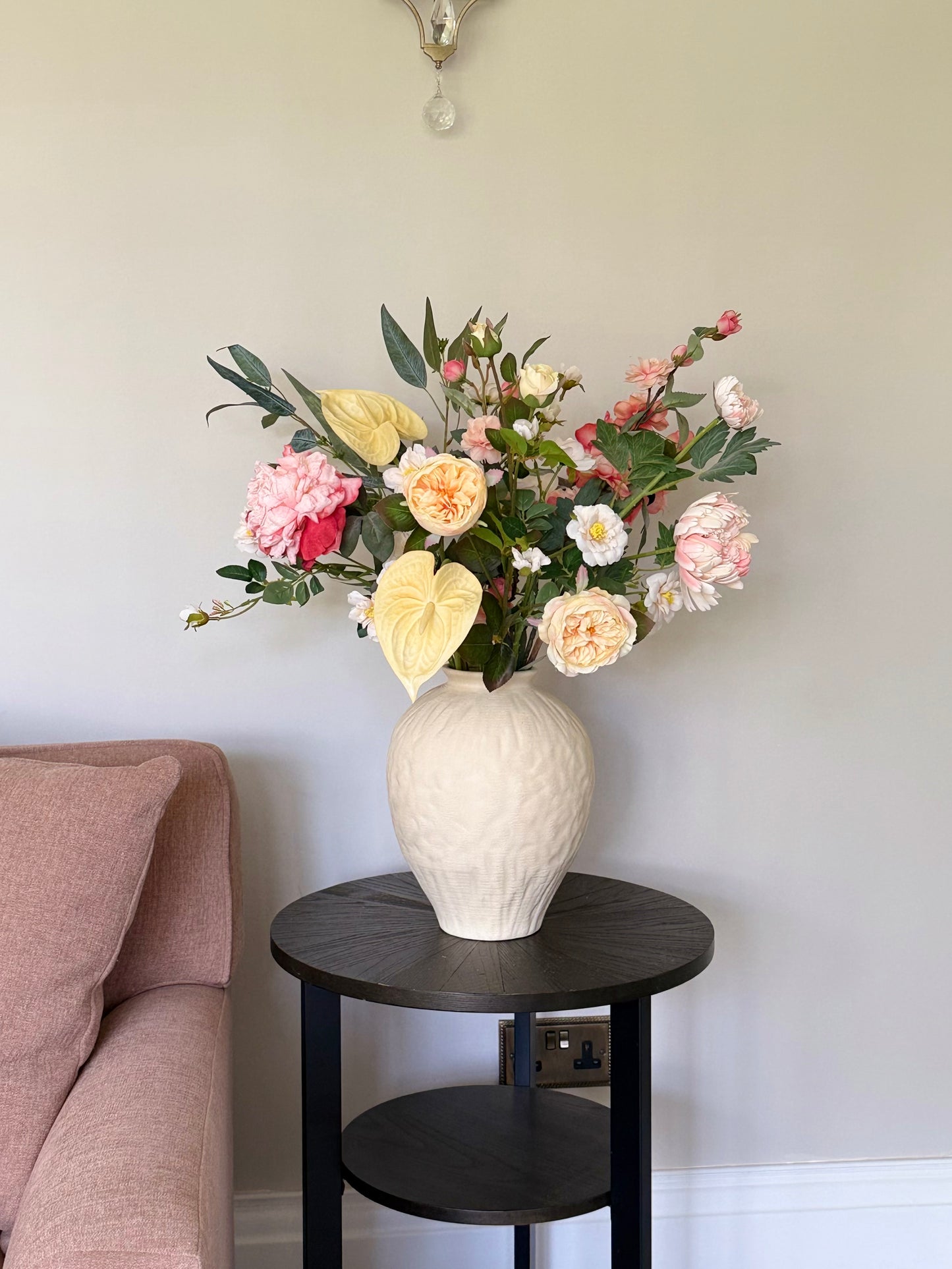 Peachy Faux Floral arrangement in a white vase on a black side table against a light wall.
