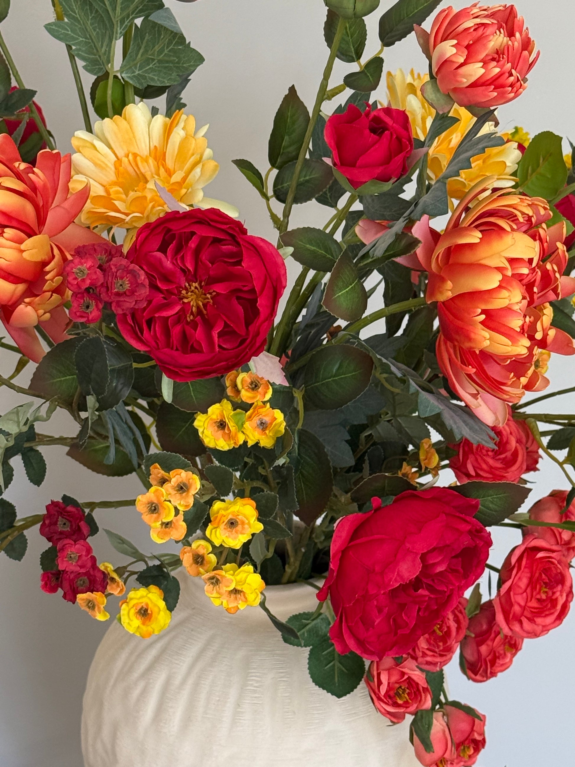 Bouquet of red, yellow, and orange flowers with green leaves on a light background