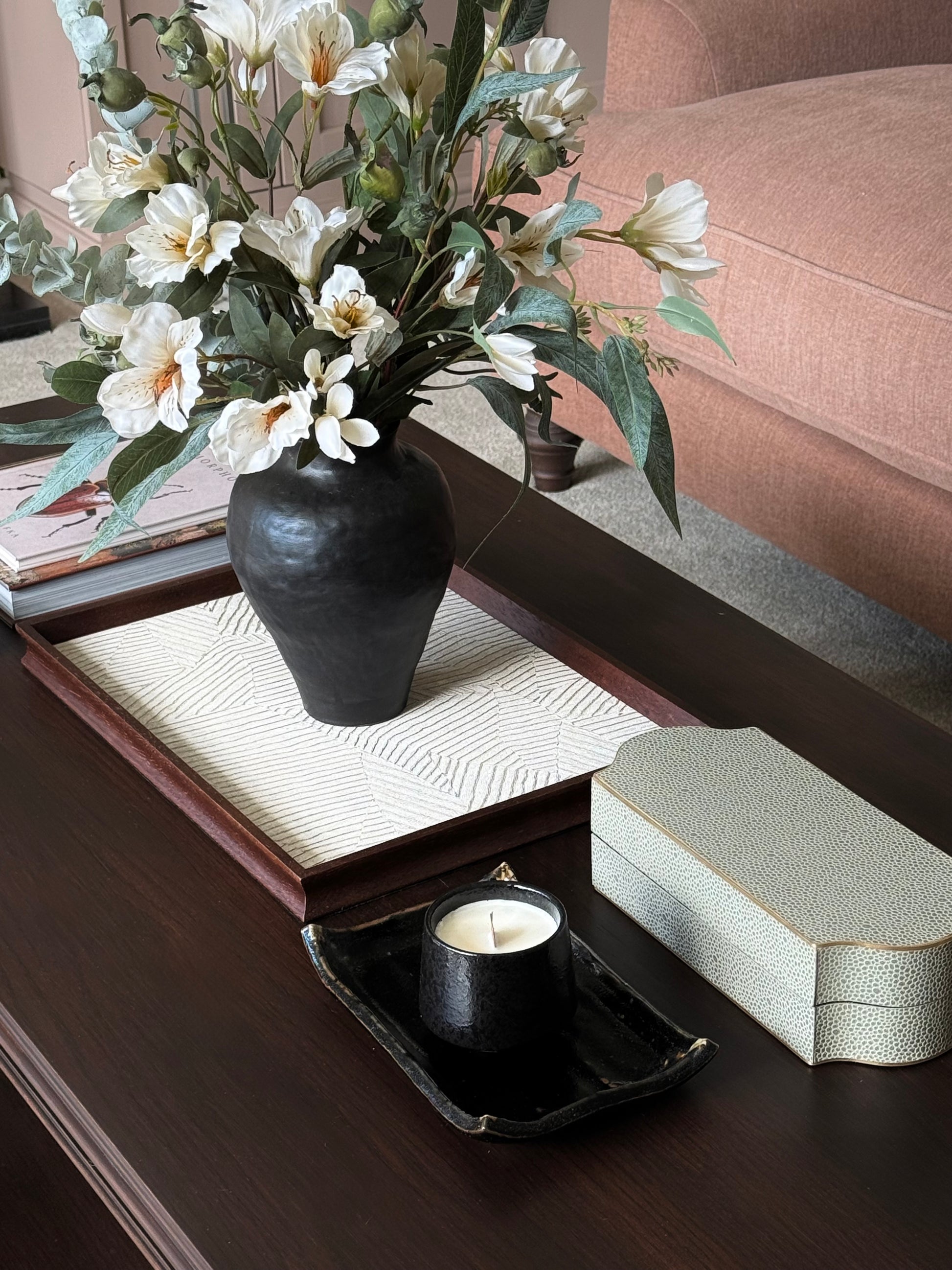 Decorative coffee table setting with a vase of flowers, candle, and box on a wooden surface.