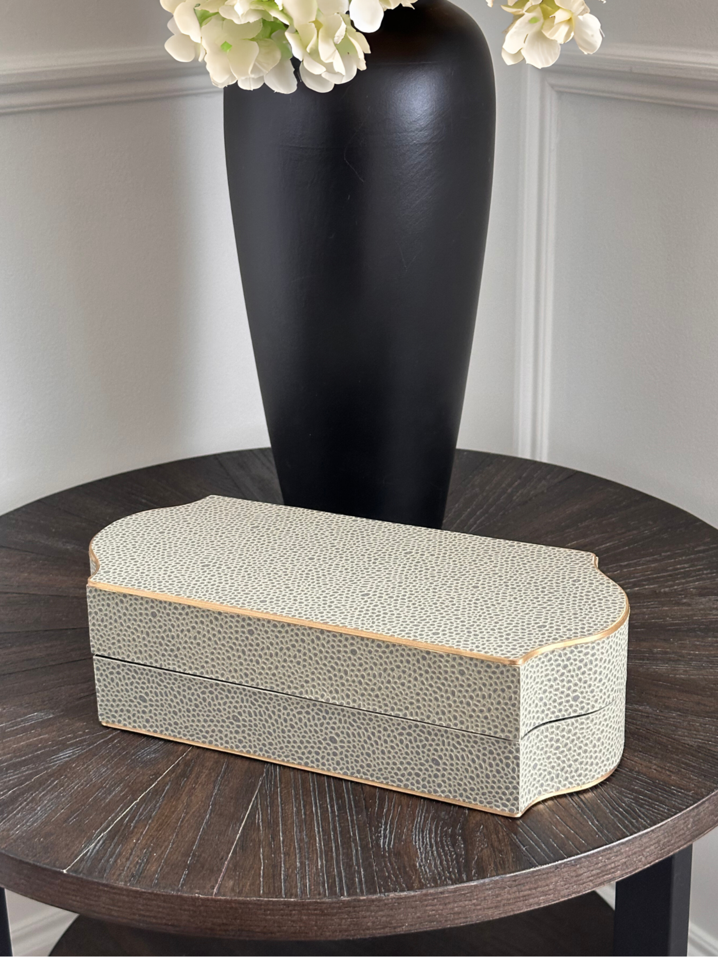 Decorative box with textured surface on a wooden table next to a black vase and white flowers.