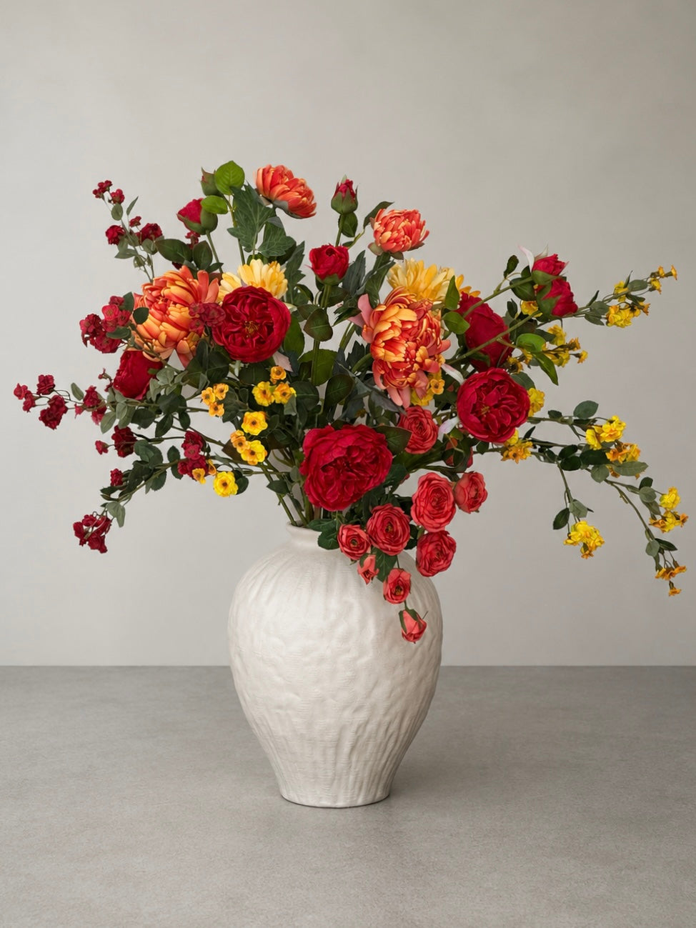 Bouquet of red, orange, and yellow flowers in a white textured vase on a light gray background