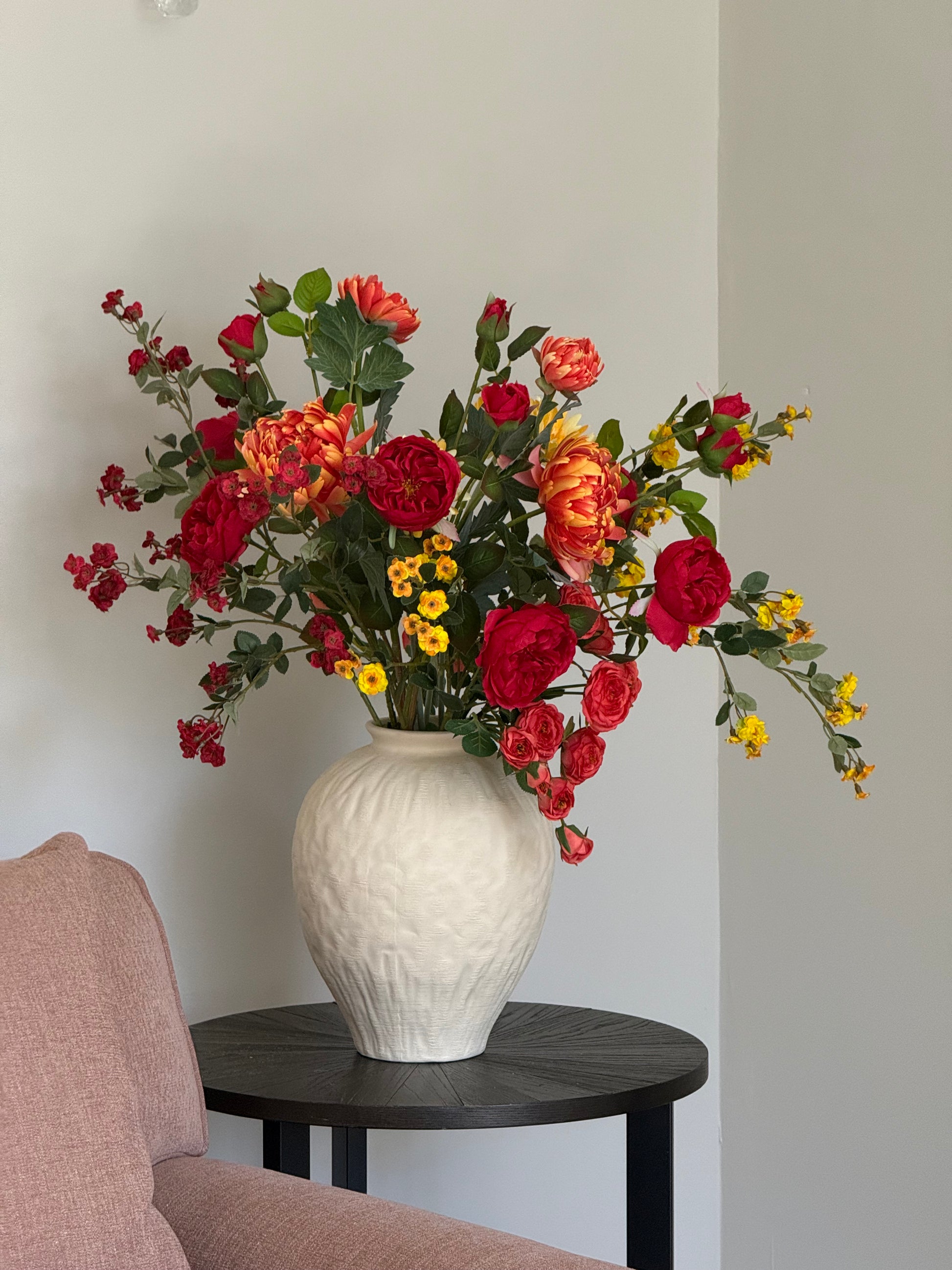 Bouquet of red and orange flowers in a white vase on a light gray surface.