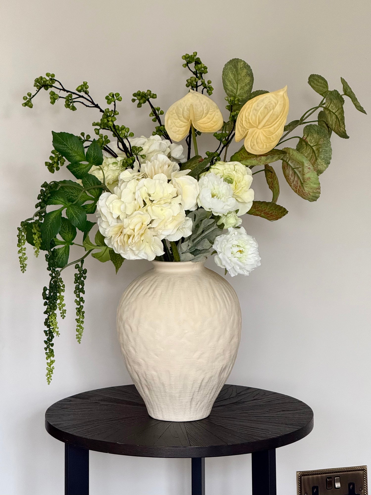 White vase with artificial faux flowers on a black table against a white wall