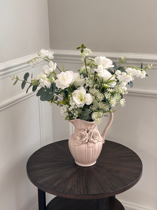 vintage vase with white faux flowers on a dark wooden table against a light gray wall.