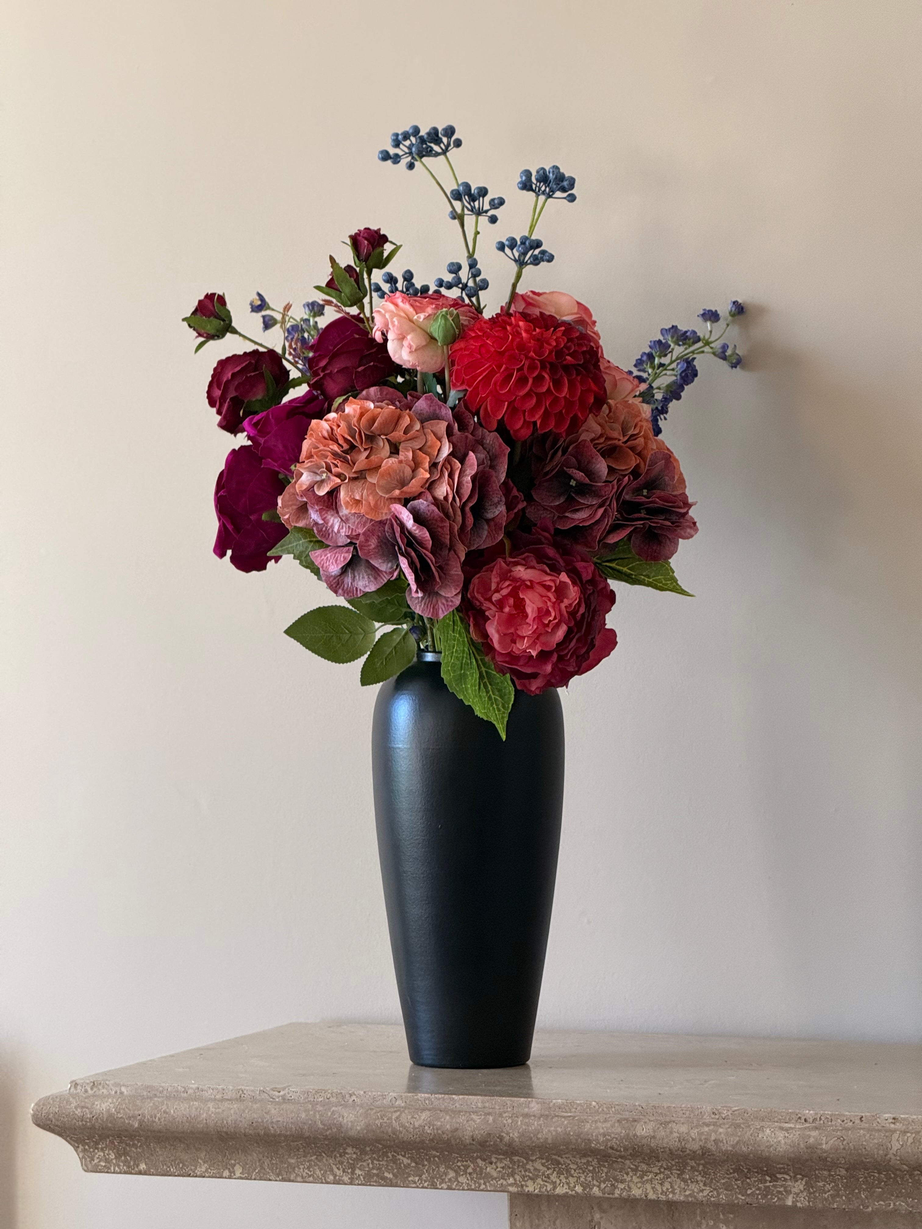 Bouquet of artificial flowers in a black vase on a stone surface with a neutral background