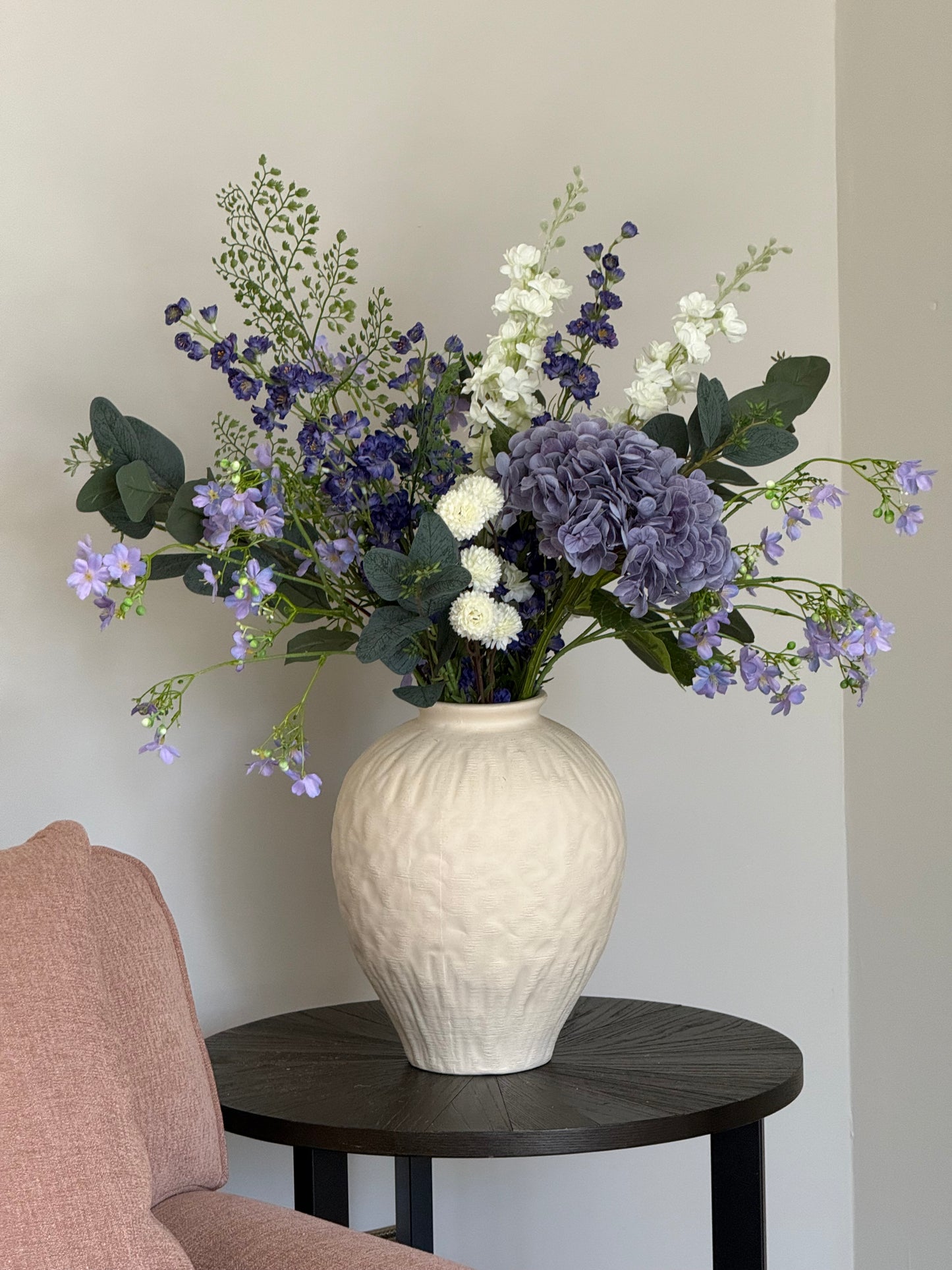 Bouquet of flowers with a textured white vase on a light surface.