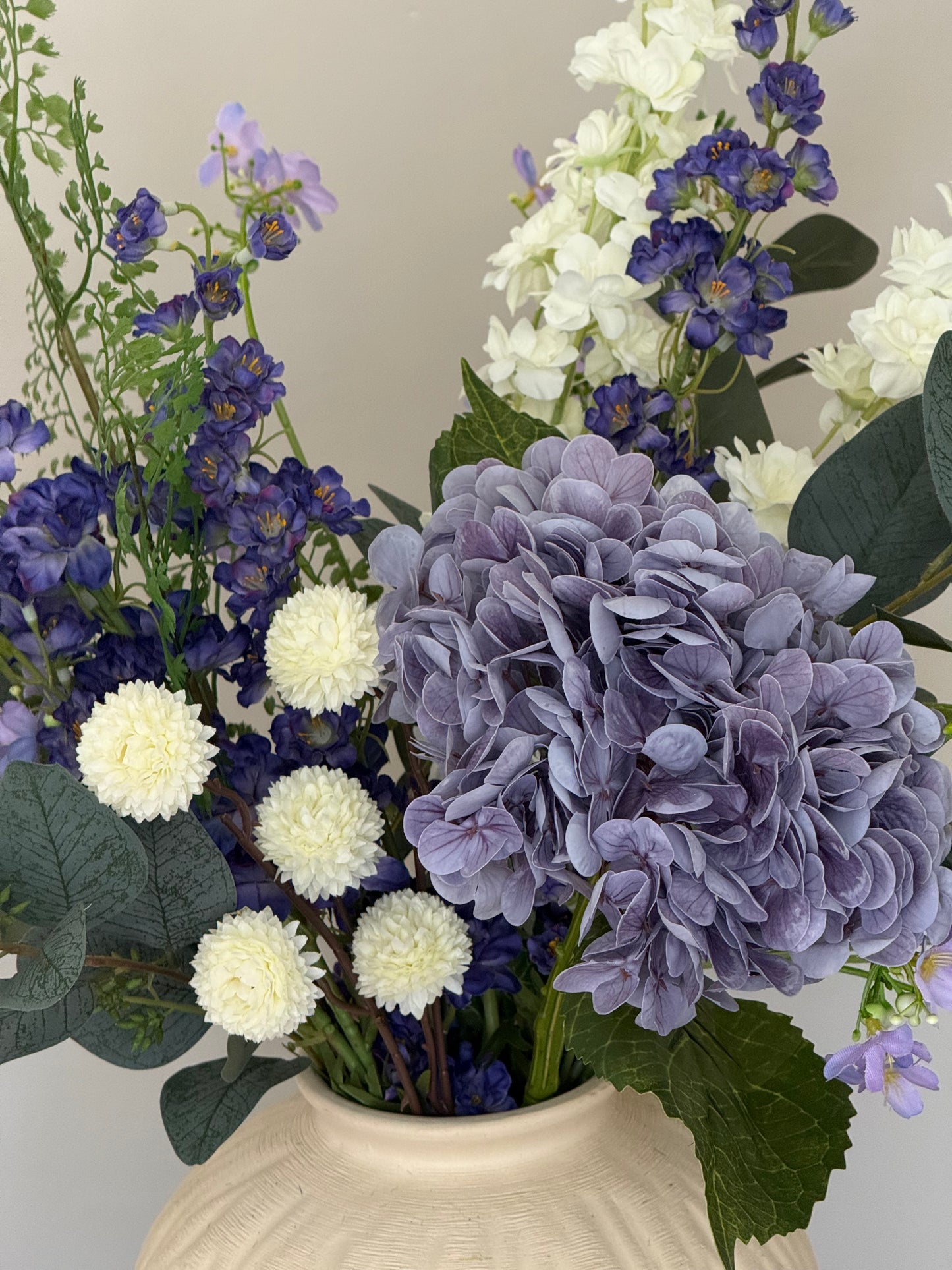 Bouquet of purple and white flowers with green leaves in a beige vase.