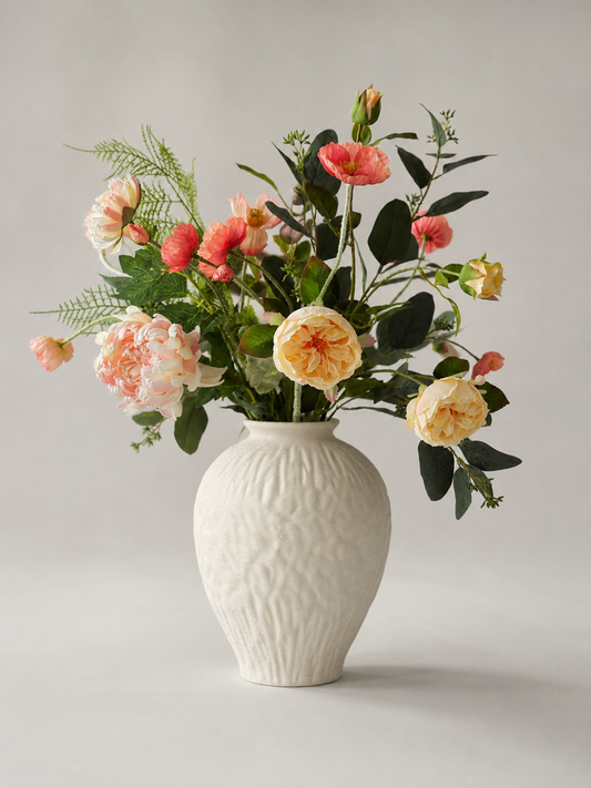 White textured ceramic vase with a bouquet of  peach flowers on a light gray background