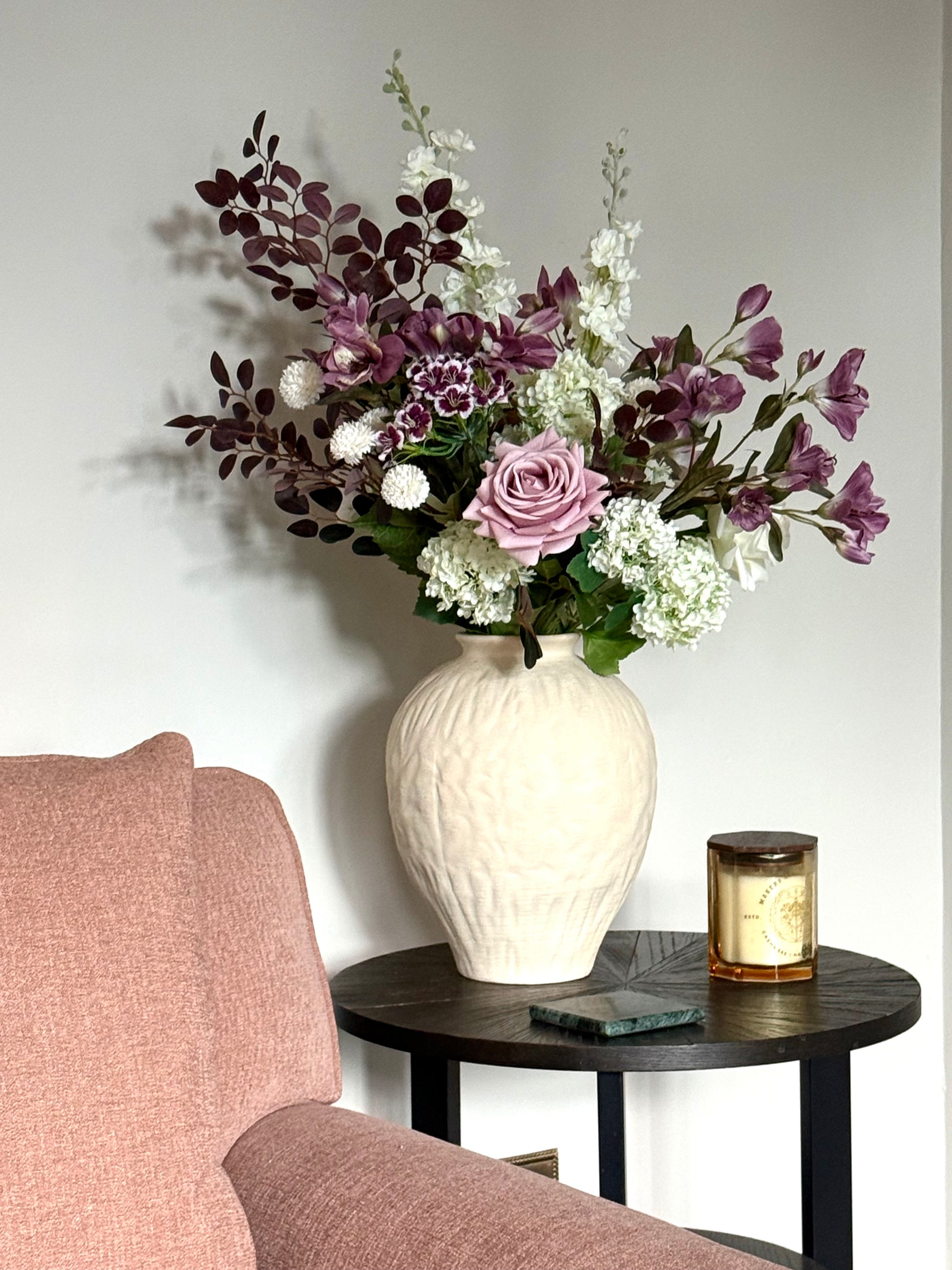 Floral arrangement in a white vase on a side table next to a chair.