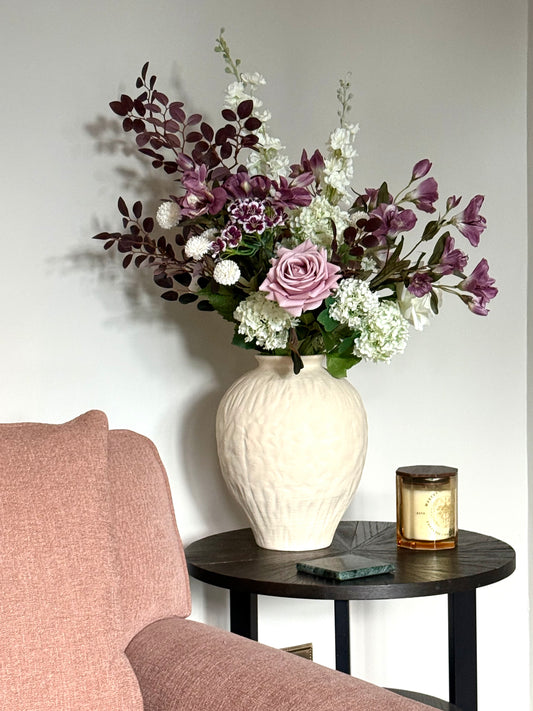 Floral arrangement in a white vase on a side table next to a chair.