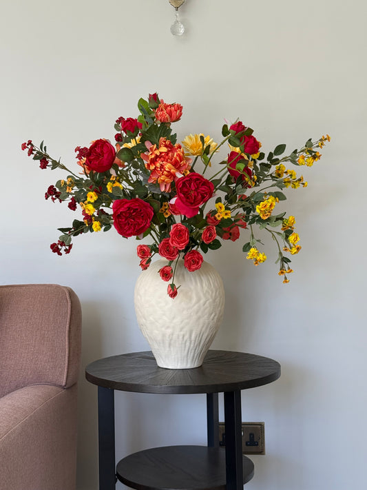 Colorful bouquet of flowers on a table with a white lamp and chair in the background.